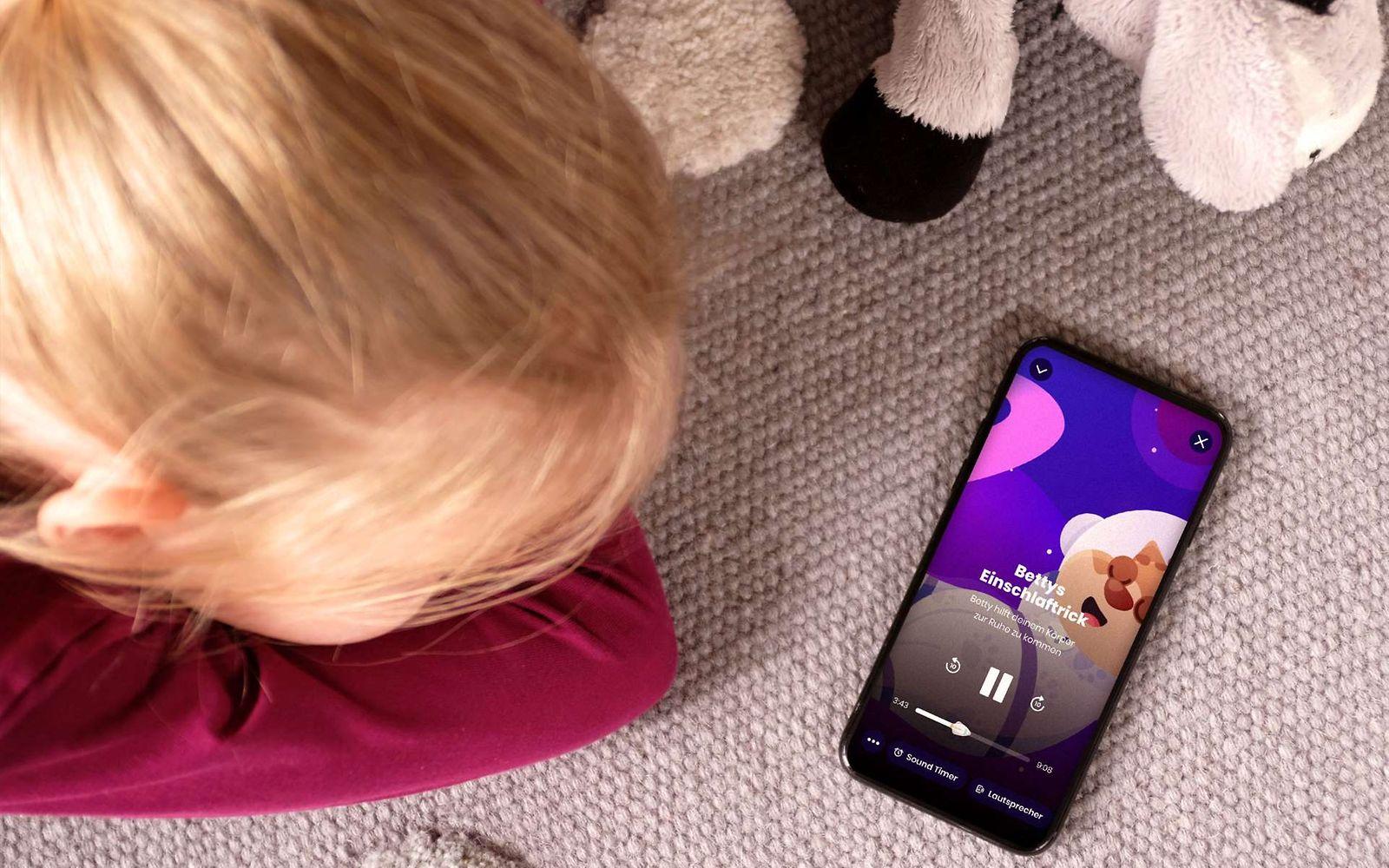 Einschlafhilfe Aumio App: Ein kleines Kind liegt auf dem Boden und lauscht einer Geschichte.